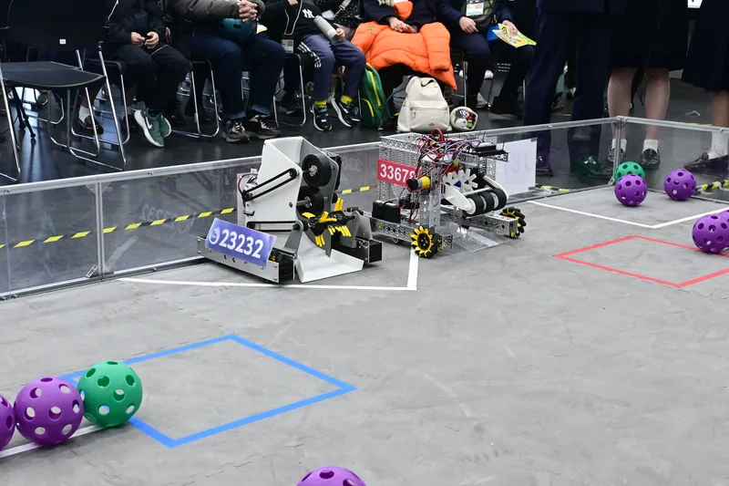 Student-built robots on the competition field, with spectators watching behind
