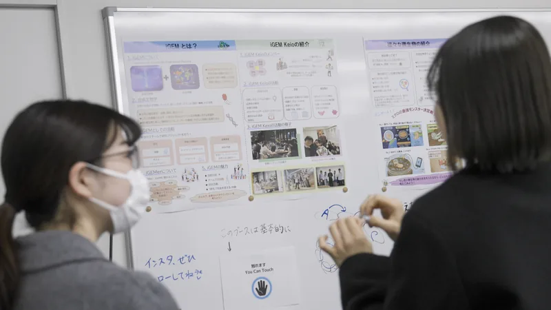 Visitors listening to an explanation of synthetic biology in front of an iGEM Keio poster