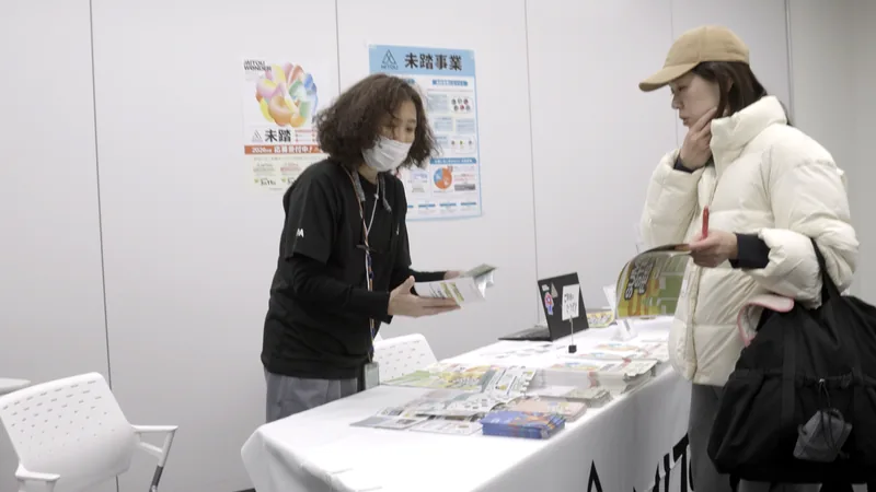 A visitor receiving a brochure at the Mitou program booth